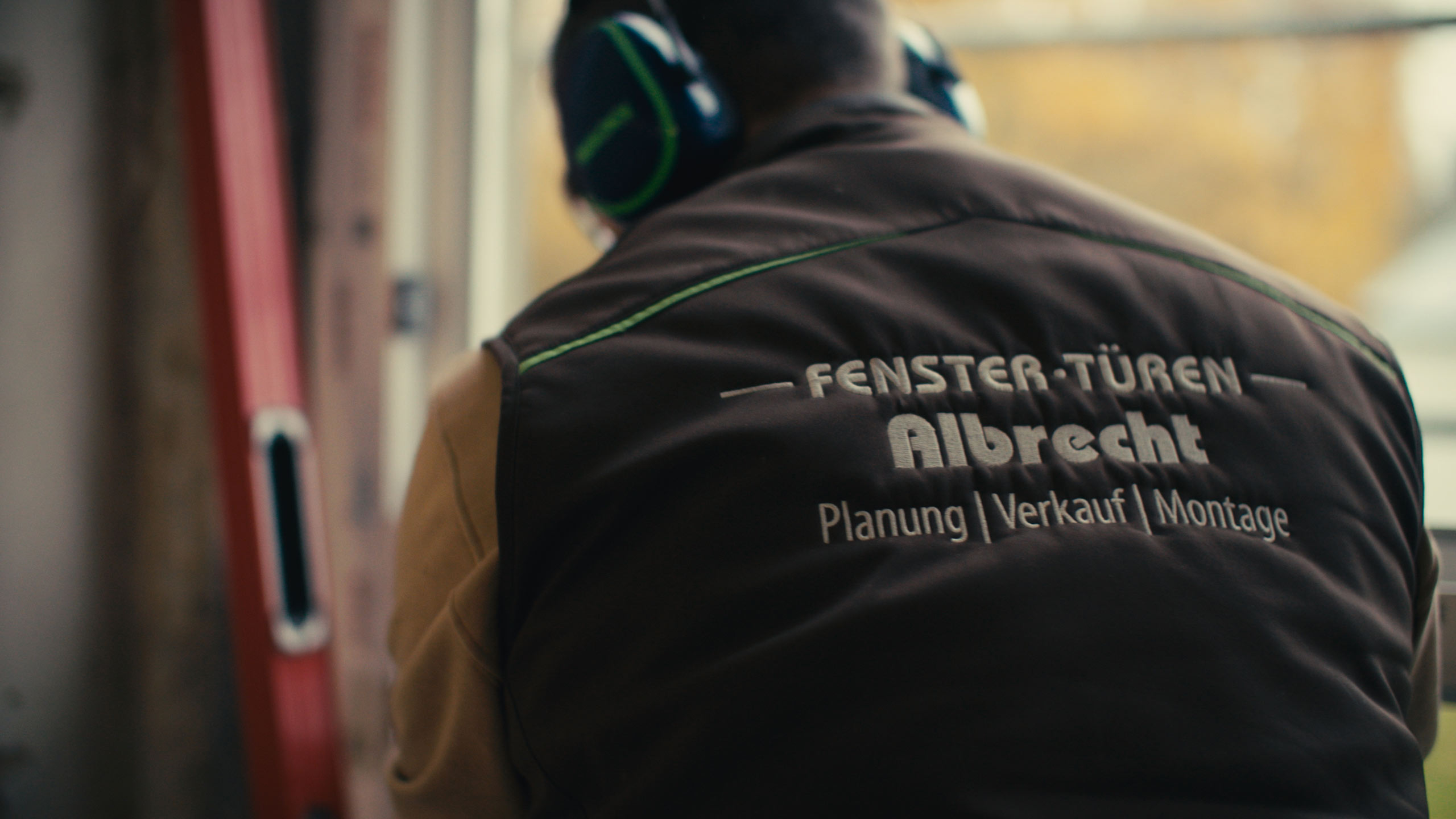 Ein Mitarbeiter der Firma Fenster-Türen Albrecht während der Arbeit von hinten abgelichtet. Auf der Arbeitskleidung ist das Logo des Unternehmens zu sehen